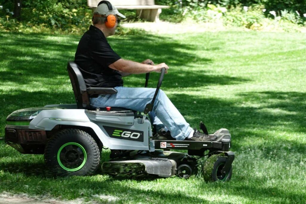 A man mows grass using a battery-powered riding lawnmower