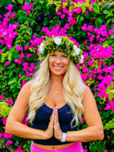 Emilee of Flow Yoga with Emilee poses in front of a green bush with bright pink flowers
